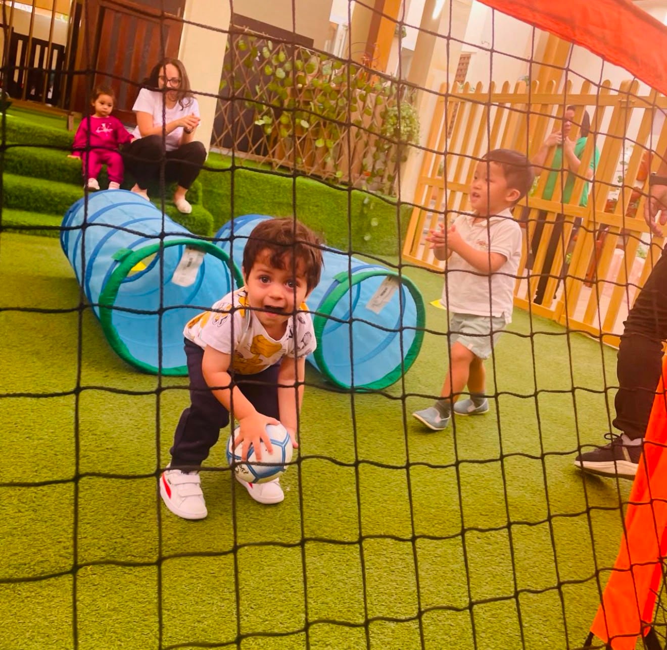 Child crawling through a play tunnel with a football during an ECA session
